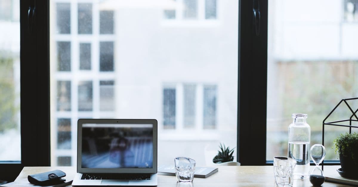Sleek office desk setup featuring a laptop, glass of water, and open window view.