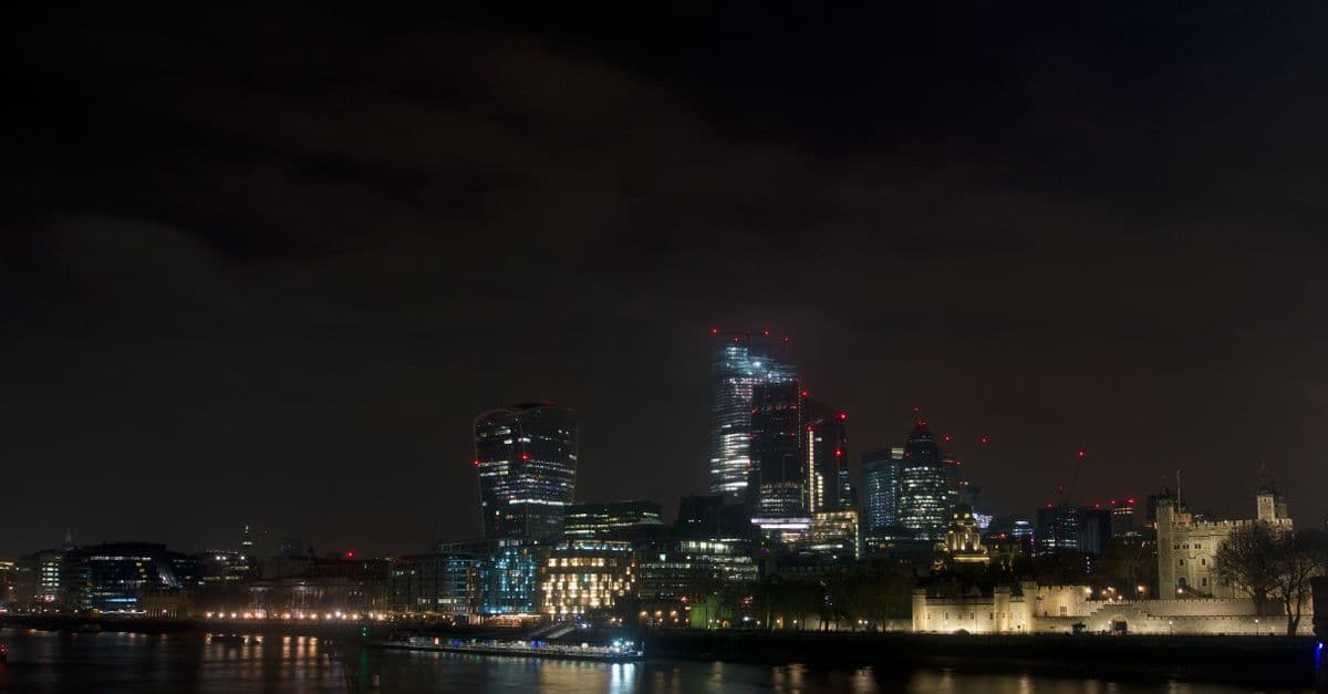 Dramatic night view of London's skyline featuring modern skyscrapers and the historical Tower of London.